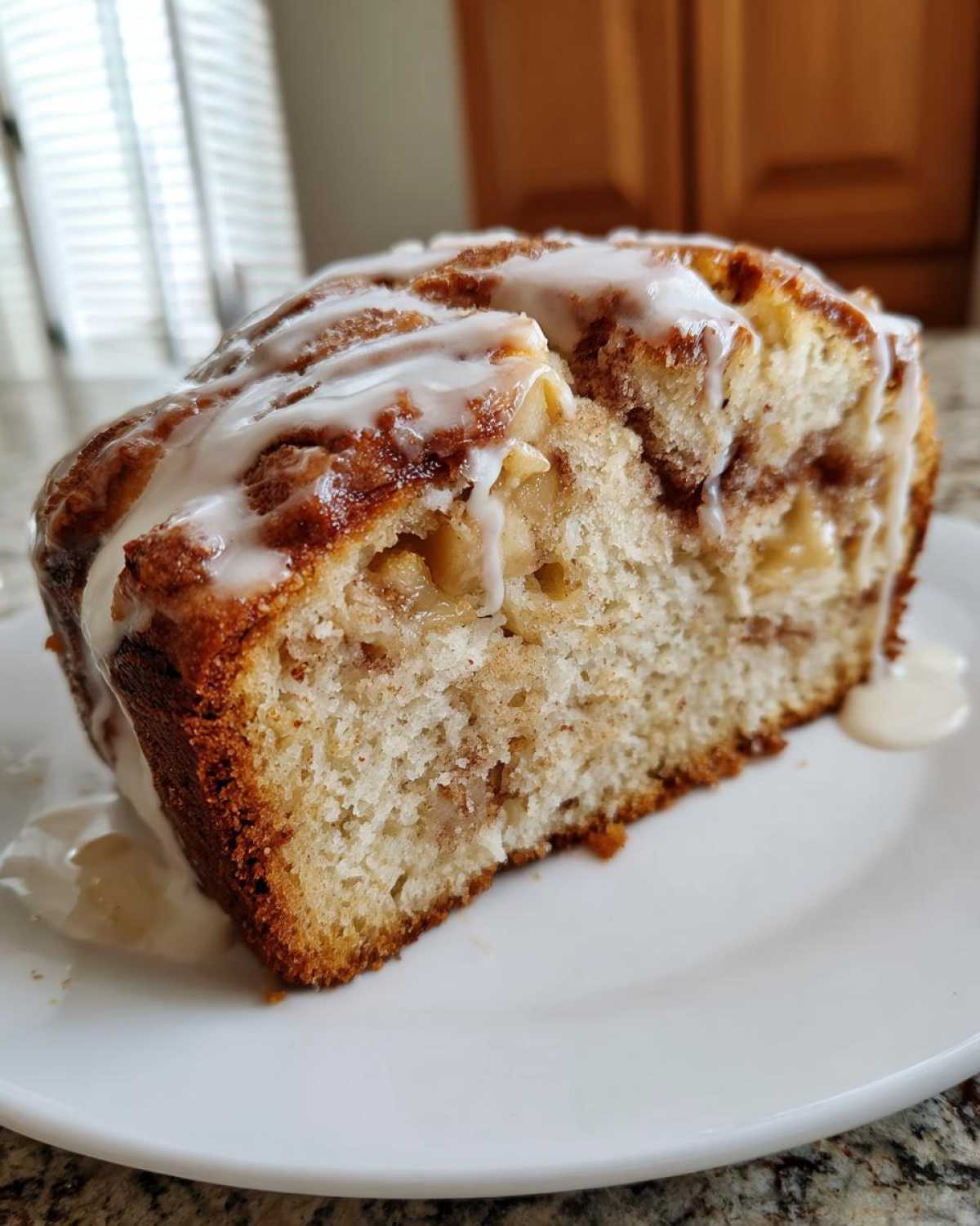 A close-up of a moist slice of apple fritter bread topped with a generous vanilla glaze.