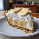 A generous slice of banana cream pie recipe featuring a graham cracker crust, creamy filling, and topped with whipped cream and fresh banana slices.
