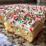 A close-up of a square slice of soft christmas sugar cookie bars topped with thick white frosting and red and green sprinkles.
