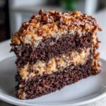 Close-up of a rich slice of german chocolate cake showing dark layers and coconut pecan frosting.