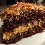 Close-up of a moist slice of german chocolate cake recipe showing dark chocolate layers and coconut-pecan filling.