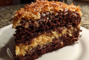 Close-up of a moist slice of german chocolate cake recipe showing dark chocolate layers and coconut-pecan filling.