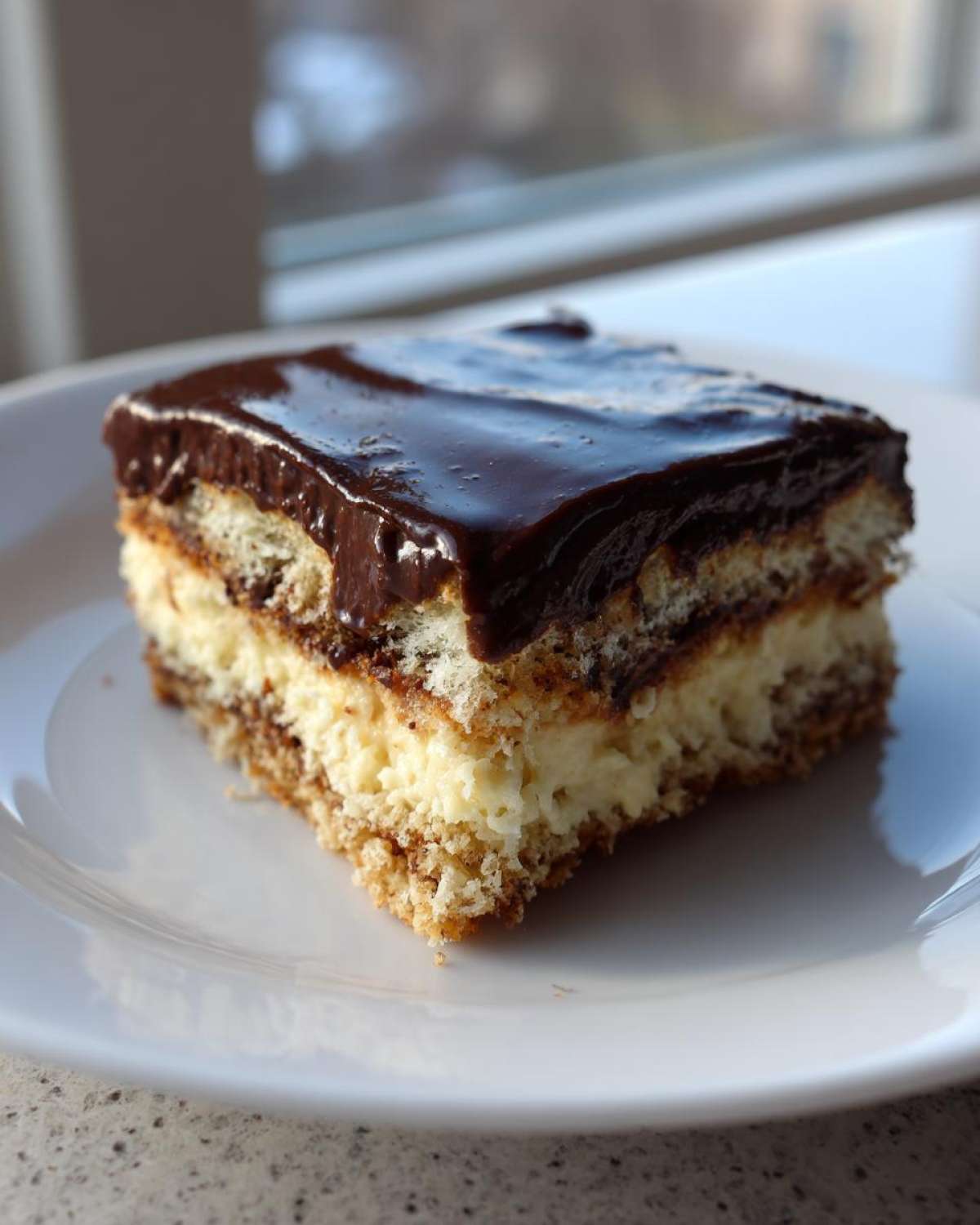 A square slice of eclair cake featuring layers of pastry, cream filling, and topped with glossy chocolate ganache.