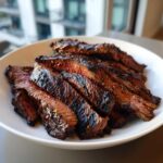 Close-up of medium-rare sliced steak, glistening from the carne asada marinade, served on a white plate.