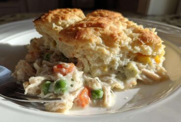 A serving of creamy slow cooker chicken pot pie topped with a golden biscuit, featuring shredded chicken, peas, and carrots.