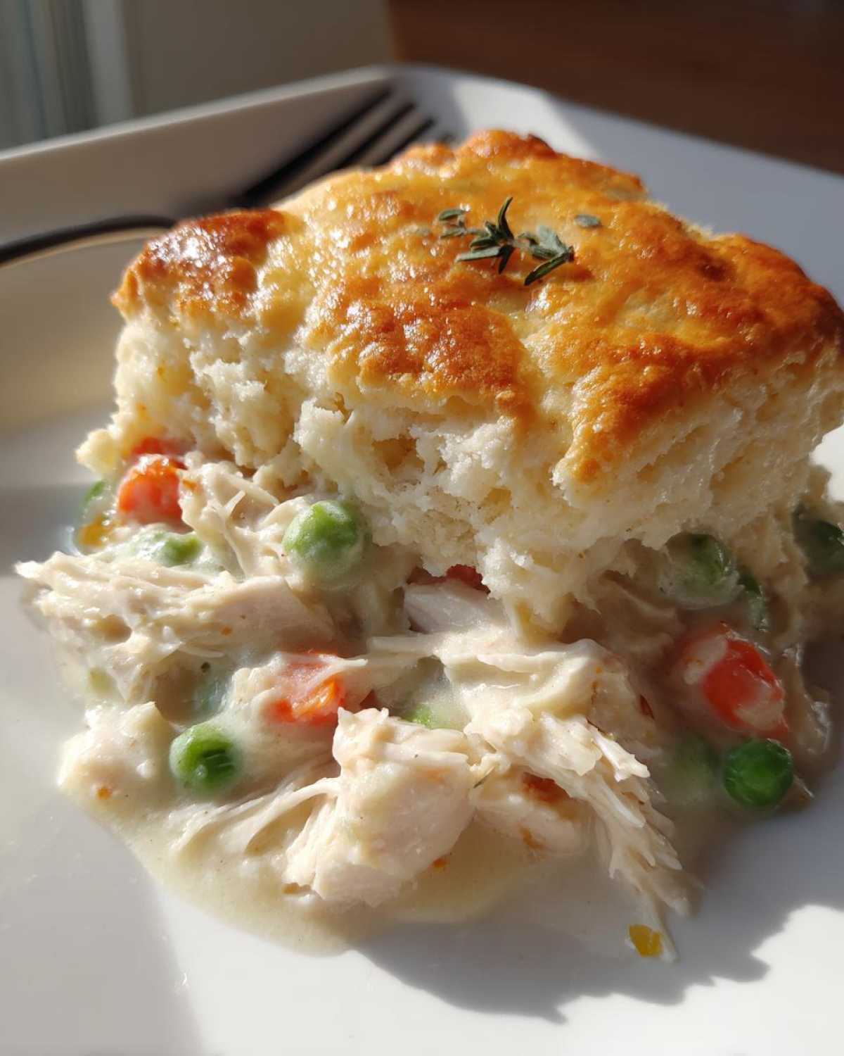 A close-up of a serving of slow cooker chicken pot pie featuring shredded chicken, peas, and carrots in a creamy sauce, topped with a golden, flaky biscuit.
