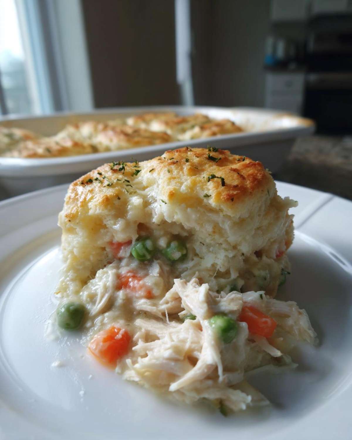 A serving of creamy slow cooker chicken pot pie featuring shredded chicken, peas, and carrots under a fluffy biscuit topping.