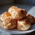A close-up stack of soft, chewy snickerdoodles generously coated in cinnamon sugar, resting on a white plate.