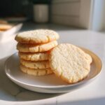 A stack of five soft sugar cookies with one leaning against the side on a white plate.