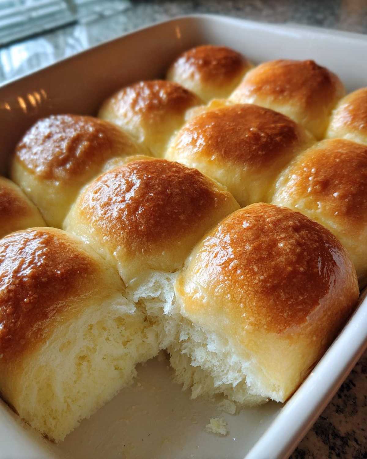 Close-up of fluffy, golden-brown sourdough discard rolls baked together in a white dish, one roll pulled apart.