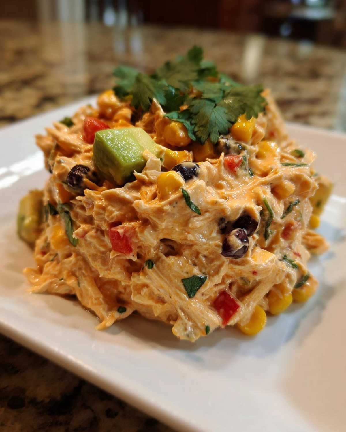 A scoop of creamy southwest chicken salad mixed with corn, black beans, and topped with avocado and cilantro.