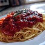 Close-up of spaghetti topped generously with thick, rich tomato sauce and garnished with herbs.