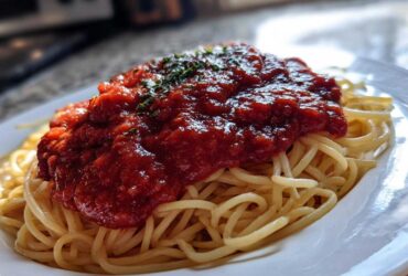 Close-up of spaghetti topped generously with thick, rich tomato sauce and garnished with herbs.