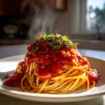 A mound of spaghetti topped generously with steaming, rich tomato sauce and fresh basil.