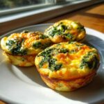 Three golden brown egg muffins topped with spinach and melted cheese, ready for breakfast.