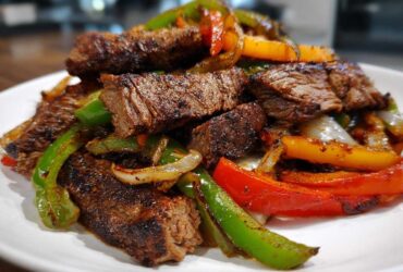 Close-up of seasoned, sliced steak mixed with colorful sautéed peppers and onions for steak fajitas.
