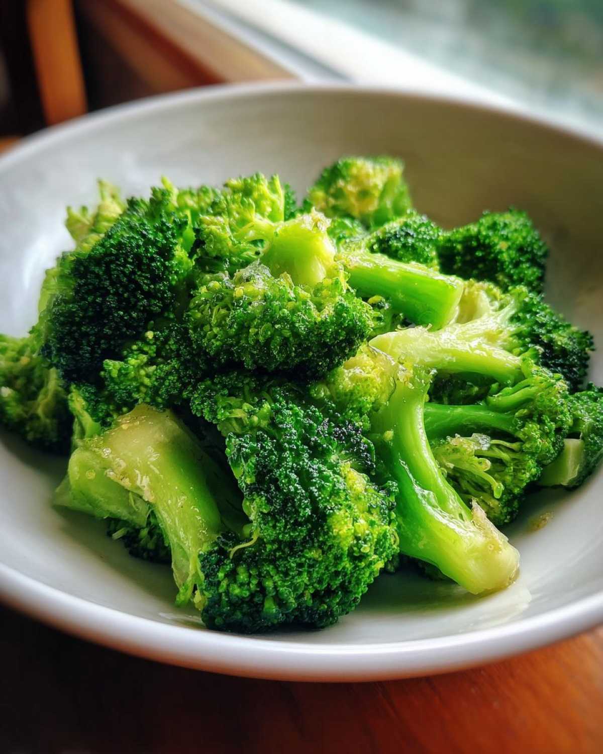 Close-up of bright green, perfectly cooked steamed broccoli florets served in a white bowl.