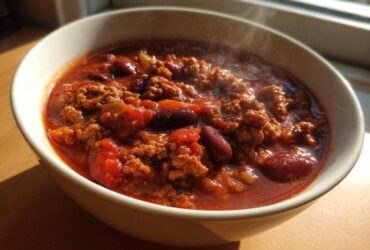 Close-up of a steaming white bowl filled with rich, red high protein chili featuring ground meat and kidney beans.