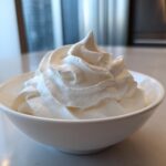 A white bowl filled with stiffly piped, bright white royal icing recipe mixture, ready for decorating.