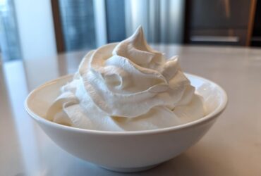 A white bowl filled with stiffly piped, bright white royal icing recipe mixture, ready for decorating.