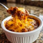 A spoonful of hot chili cheese dip showing incredible cheese pull, served in a white ramekin.