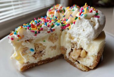 Cross-section view of a slice of sugar cookie cheesecake loaded with cookie chunks, topped with whipped cream and colorful sprinkles.