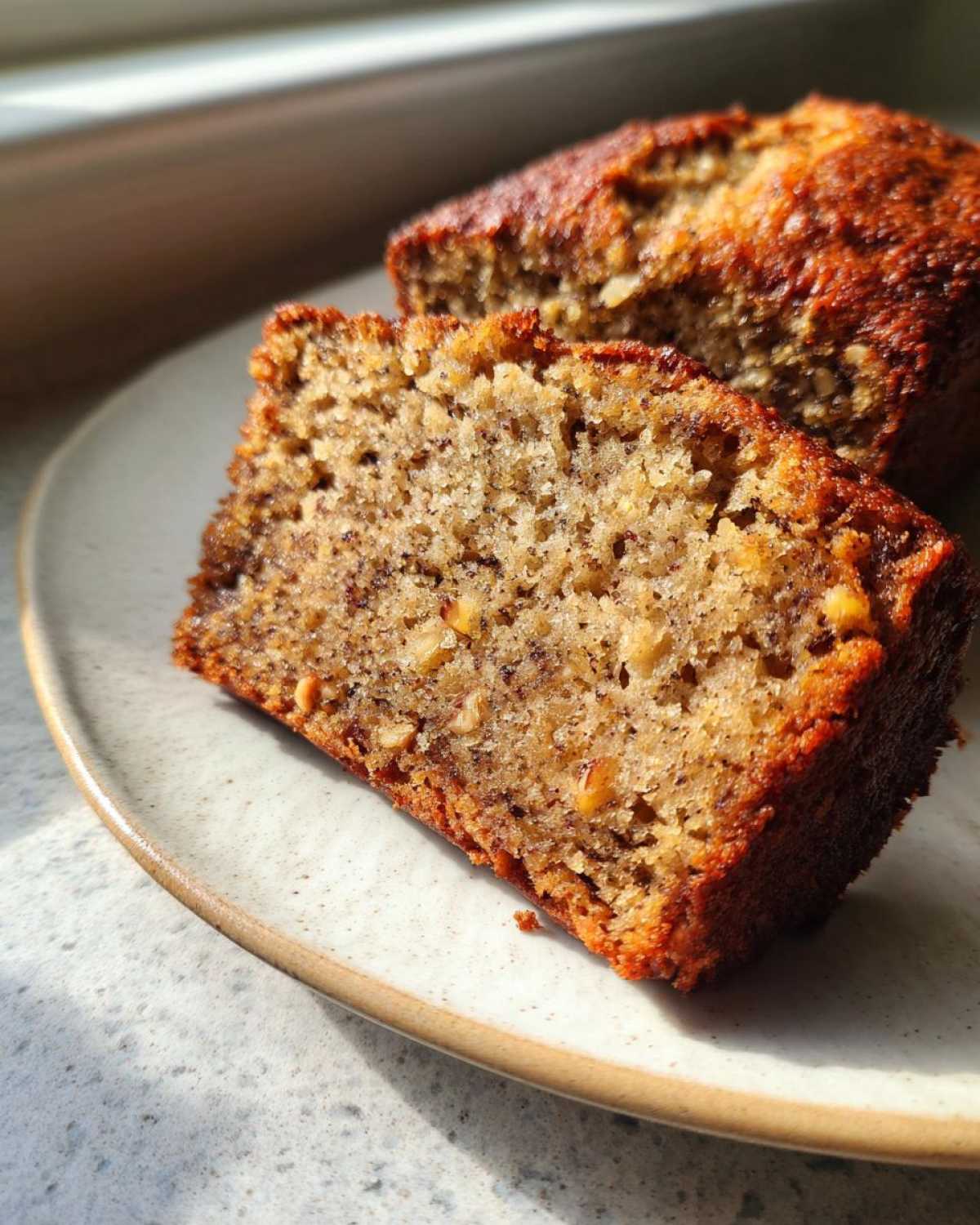 Close-up of a moist slice of sugar free banana bread with visible nuts on a speckled plate.