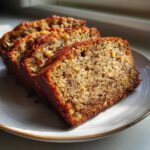 Close-up of three thick slices of moist sugar free banana bread featuring visible nuts on a light plate.