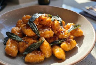 A close-up of bright orange sweet potato gnocchi tossed in sauce and topped with crispy sage leaves.