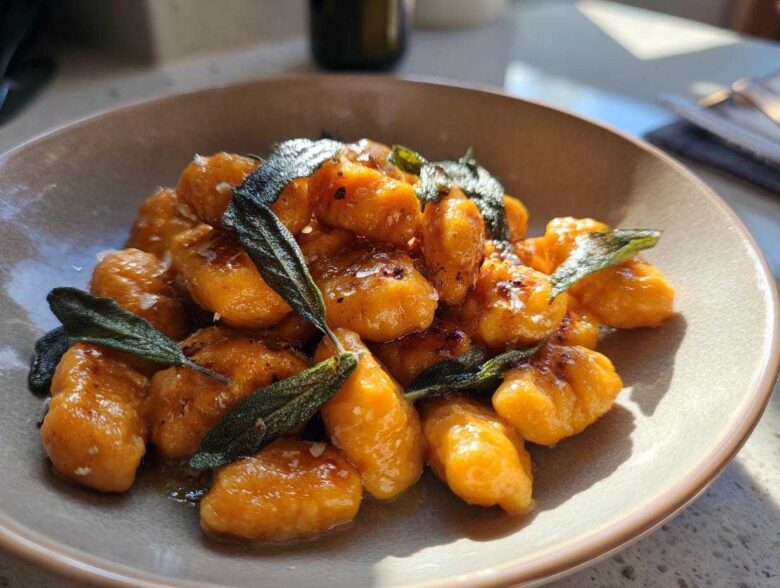A close-up of bright orange sweet potato gnocchi tossed in sauce and topped with crispy sage leaves.