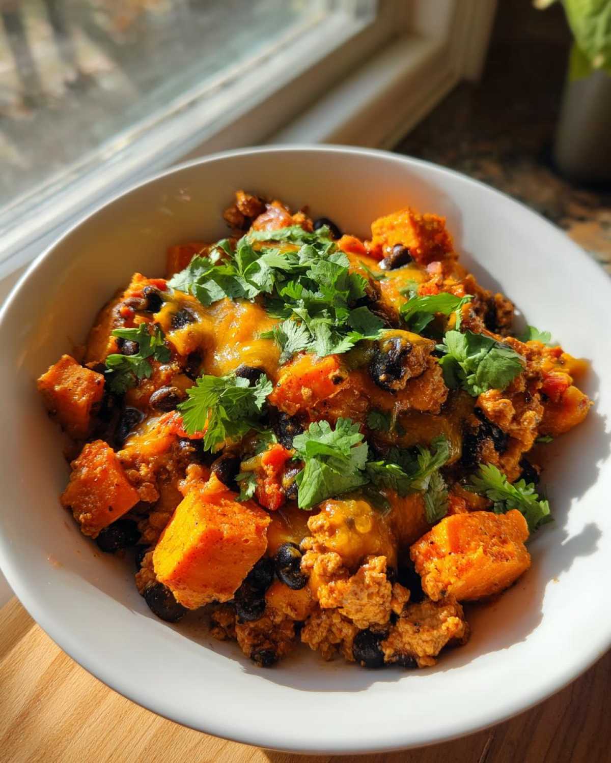A close-up of a hearty sweet potato skillet featuring orange sweet potato chunks, black beans, melted cheese, and fresh cilantro.