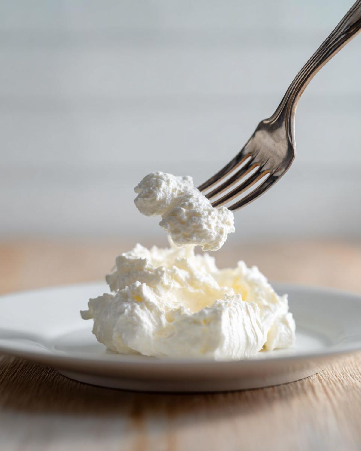 A fork lifts a dollop of thick, white, creamy ingredient, likely heavy cream or mascarpone, used for homemade alfredo sauce.