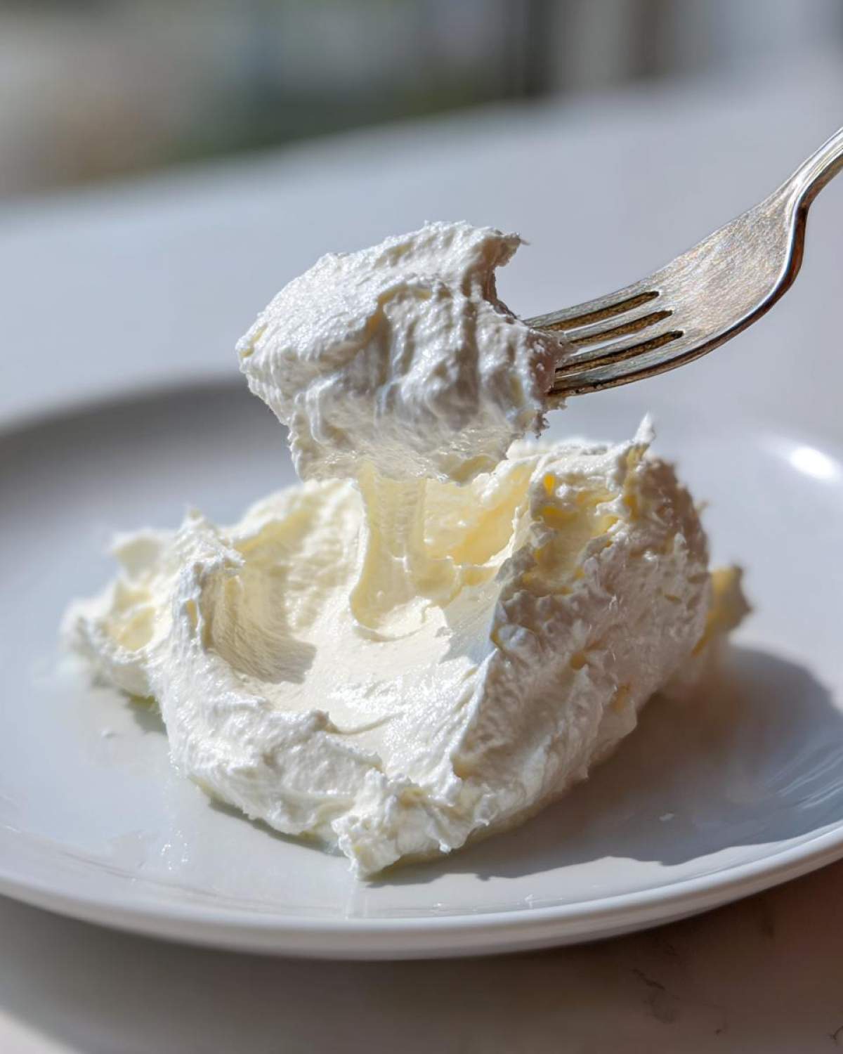 A fork lifting a dollop of thick, creamy homemade alfredo sauce from a white plate.