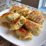 A plate of golden, pan-fried Traditional Chinese Dumplings, one cut open showing the savory filling.