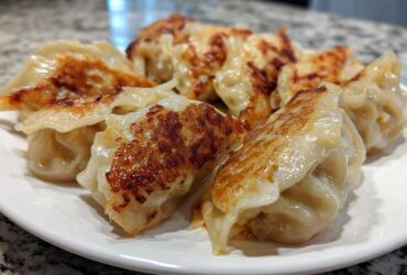 A plate of perfectly pan-fried Traditional Chinese Dumplings with golden-brown crispy bottoms.