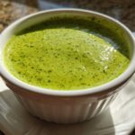 Close-up of vibrant green cilantro lime sauce served in a small white fluted ramekin on a saucer.