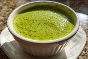 Close-up of vibrant green cilantro lime sauce served in a small white fluted ramekin on a saucer.