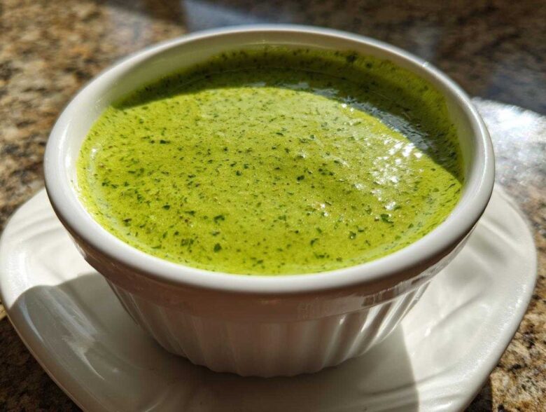 Close-up of vibrant green cilantro lime sauce served in a small white fluted ramekin on a saucer.