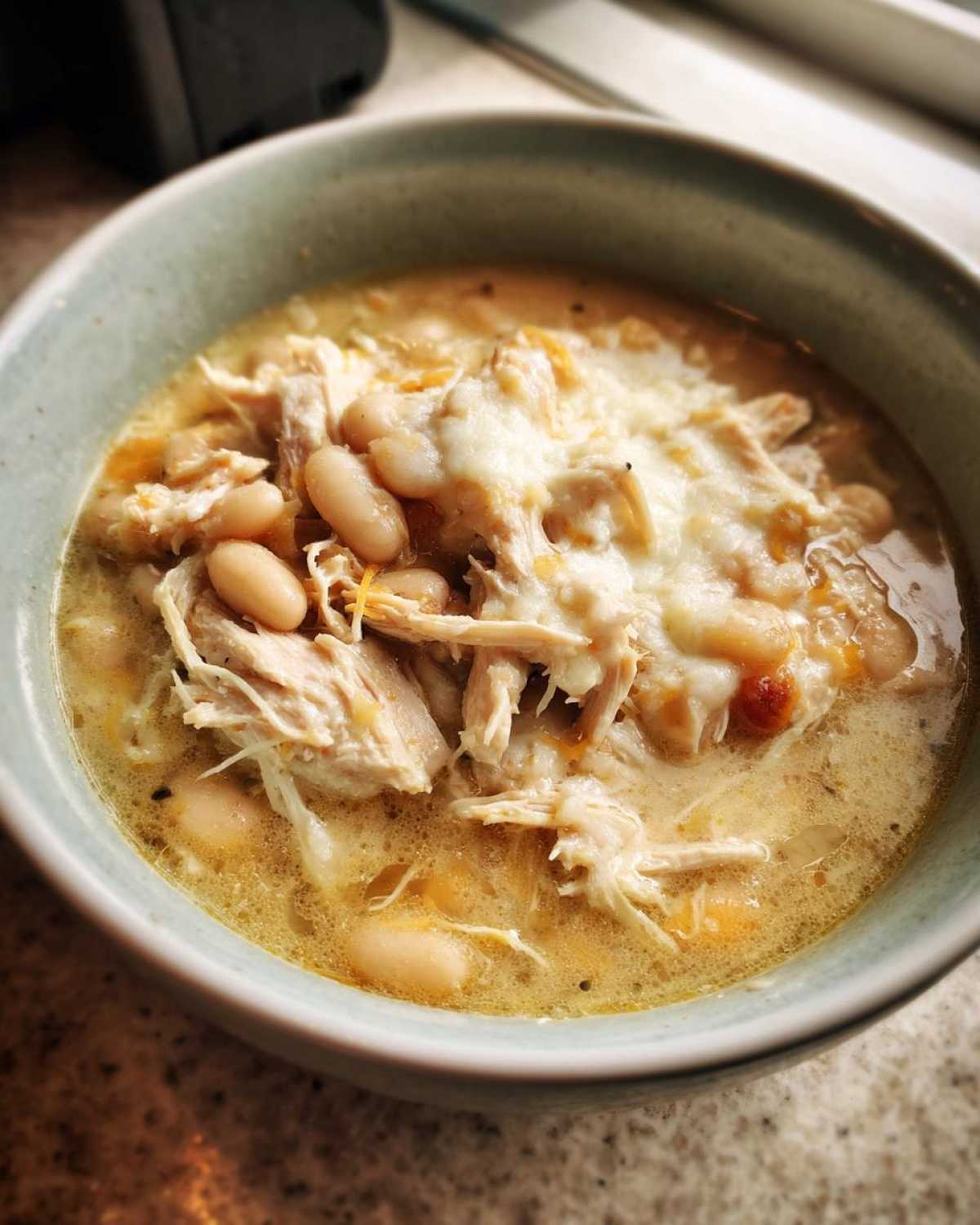 Close-up of a bowl of creamy white bean chicken chili topped with shredded melted cheese.