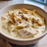 Close-up of a bowl of rich white chicken lasagna soup with chunks of chicken and noodles.