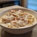 A close-up of a white bowl filled with rich white chicken lasagna soup, featuring chunks of chicken and noodles in a creamy sauce.