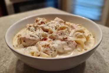 A close-up of a white bowl filled with rich white chicken lasagna soup, featuring chunks of chicken and noodles in a creamy sauce.