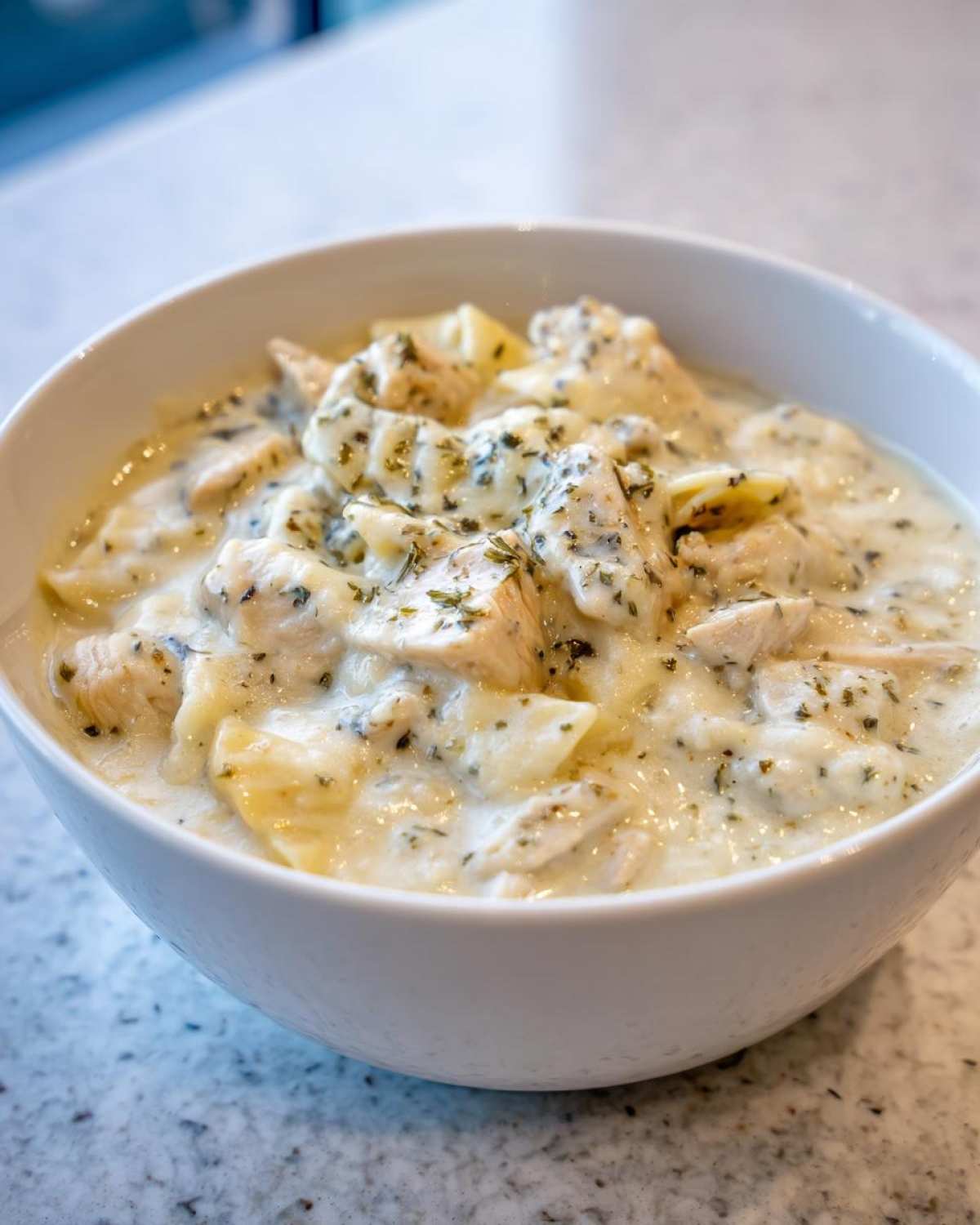Close-up of a white bowl filled with creamy white chicken lasagna soup, topped with herbs.