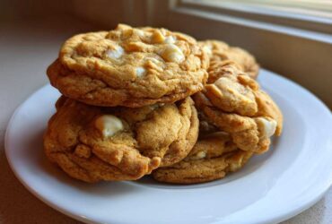 A stack of freshly baked, golden brown white chocolate macadamia nut cookies on a white plate.