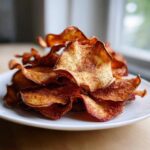 A close-up of crispy Air Fryer Cinnamon Sugar Apple Chips piled high on a white plate.