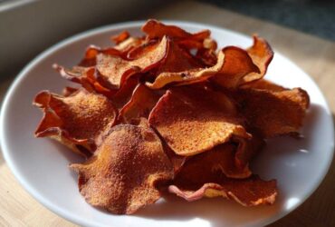 A pile of crispy, reddish-brown Air Fryer Cinnamon Sugar Apple Chips dusted with sugar on a white plate.