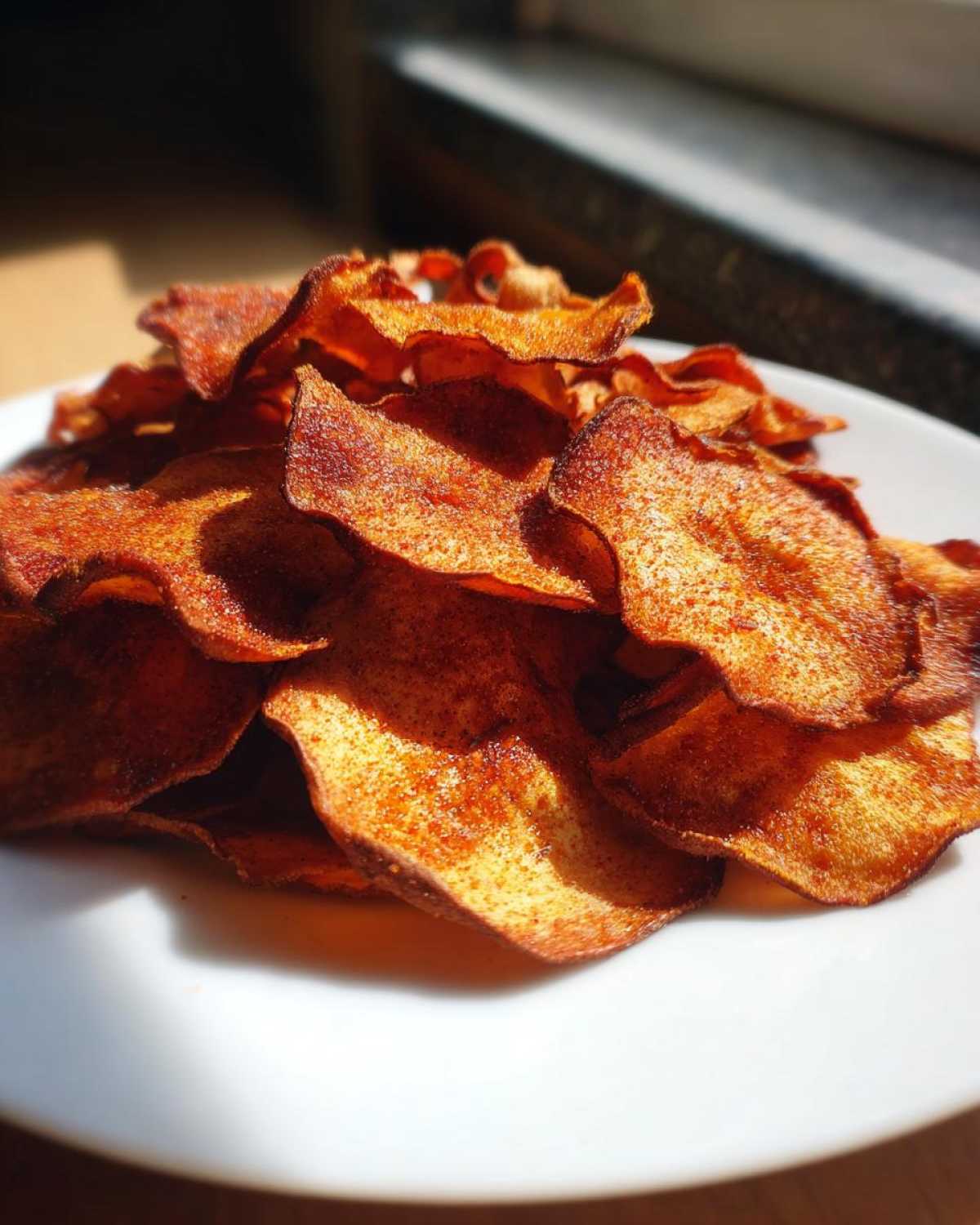 A close-up of crispy, golden-brown Air Fryer Cinnamon Sugar Apple Chips piled high on a white plate.