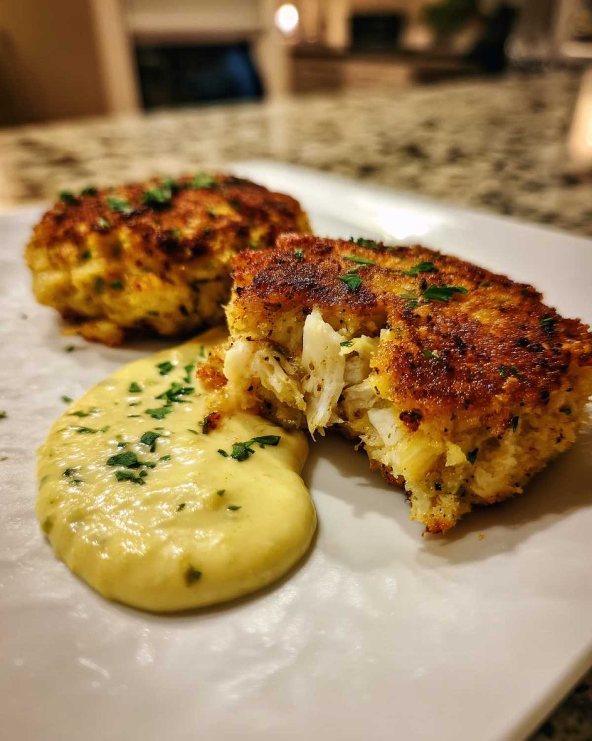 Close-up of Air Fryer Crispy Crab Cakes, one broken open showing flaky crab meat next to lemon aioli.