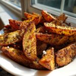 A bowl overflowing with golden brown Air Fryer Crispy Rosemary Potato Wedges seasoned with herbs.