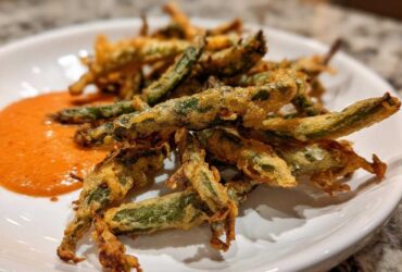 A plate of golden brown Air Fryer Crispy Tempura Green Beans served with a side of orange dipping sauce.